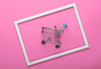 Mini shopping trolley on pink background with white frame. Studio shot. Creative flat lay. Top...
