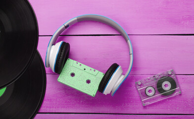 Stereo headphones with audio cassette, vinyl records on pink wooden table. Music lover. Retro 80s. Top view.