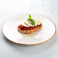 Italian bruschetta with roasted tomatoes, vegetables, mozarella and basil on a plate