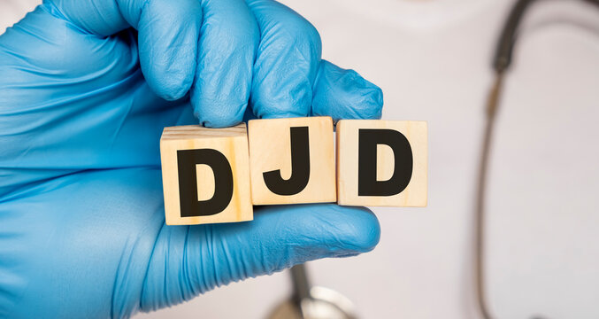 DJD Degenerative joint disease - word from wooden blocks with letters holding by a doctor's hands in medical protective gloves. Medical concept.