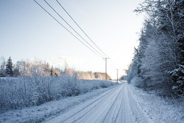 A beautiful winter day landscape of a gravel road near the forest. Snow covered scenery of Northern Europe.