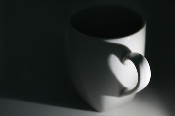 White coffee cup with shadow from handle in heart form on black background. Horizontal, copy space