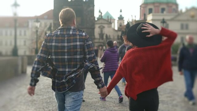 Sweet couple have romantic time while honeymoon trip in old european city of Prague. Young lovers holding hands running on street and kissing.