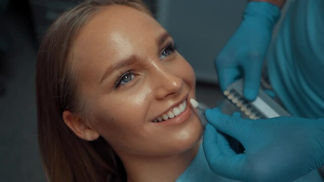 A male dentist uses a teeth whitening table to select a color for a smiling patient. Dental treatment and care. Oral hygiene. Health care and medicine concept.