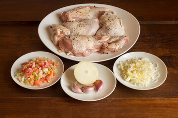 Presentation of raw ingredients to plate the preparation of chicken recipe in vegetable sauce on rustic chestnut wood background. Food, meat, and vegetables.