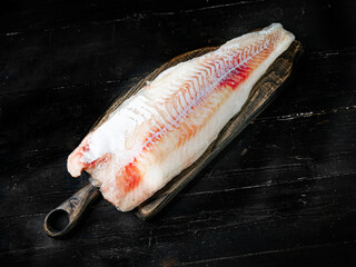 Fresh codfish fillet on a wooden cutting board. Top view. 