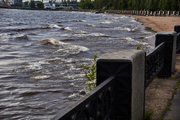Panorama of the embankment by the lake.Along the sandy shore of the lake, there is a granite embankment, which is fenced with a cast-iron fence with pedestals. On the lake, the wind raised waves.