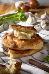 A stack of pita bread on a striped towel, garlic, onion and celery