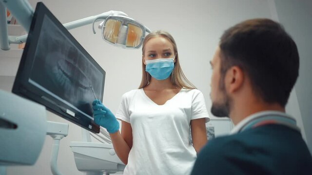 Doctor dentist in gloves show the teeth panoramic x-ray on digital screen in dental clinic on light background with medical equipment. Smile healthy teeth concept.