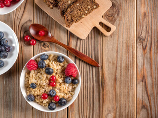 Top view of porridge with blueberries and raspberries on wooden background. Vegan breakfast.