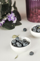 Bowls of fresh blueberries , purple jar and viola on white background
