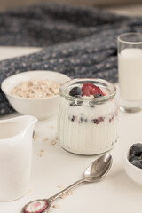 Homemade yogurt with berries in glass jar on white background. Raw dessert concept