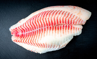 Fresh tilapia fish fillet on a black plate. Tilapia scales. Texture of striped fish scales. Macro shoot. 