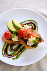 Toasted baguette toast with pesto sauce, a slice of Parma ham, mozzarella, tomato and avocado