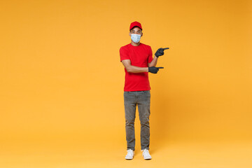 Naklejka premium Full length delivery employee african man in red cap t-shirt face mask gloves uniform work courier dealer service on quarantine coronavirus covid-19 virus concept isolated on yellow background studio.