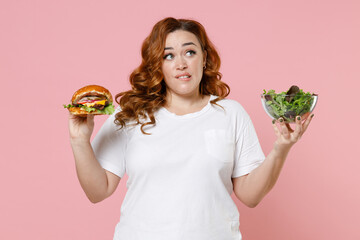 Puzzled young redhead plus size body positive woman 20s in white casual t-shirt hold american...