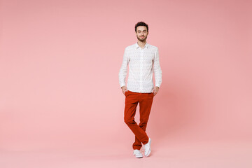 Fototapeta na wymiar Full length of smiling handsome young bearded man 20s wearing basic casual white shirt standing holding hands on pockets looking camera isolated on pastel pink color wall background studio portrait.