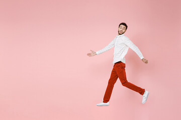 Fototapeta na wymiar Full length side view of shocked young bearded man 20s wearing basic casual white shirt jumping like running spreading hands looking camera isolated on pastel pink color background studio portrait.
