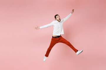 Full length of shocked amazed young bearded man 20s wearing basic casual white shirt jumping keeping mouth open spreading hands and legs isolated on pastel pink color wall background studio portrait.