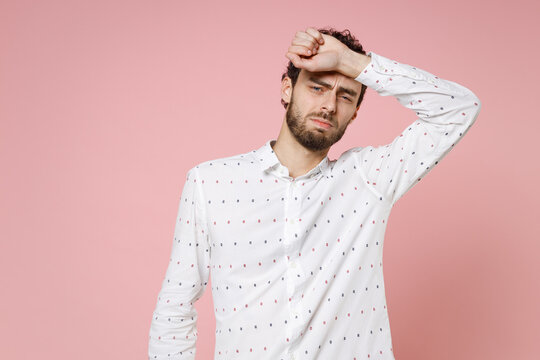 Dissatisfied exhausted tired young bearded man 20s wearing basic casual white shirt standing put hand on head looking camera isolated on pastel pink color wall background studio portrait.