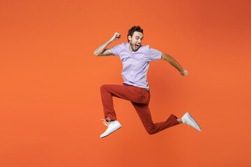 Fototapeta na wymiar Full length side view of screaming young bearded man 20s in casual violet t-shirt jumping like running keeping mouth open looking camera isolated on bright orange color background studio portrait.