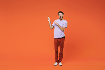 Fototapeta na wymiar Full length of amazed excited surprised young bearded man 20s in basic violet t-shirt standing pointing index fingers up on mock up copy space isolated on bright orange background studio portrait.