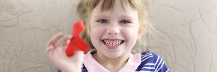Little girl smiles and holds in her hand red ribbon portrait. Having healthy children to hiv positive parents concept.