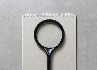 A spring notebook with a sheet of craft paper A5 with black magnifying glass on light grey concrete background. Concept of new idea, business plan and strategy. Empty space for text