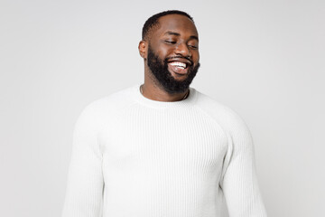 Smiling laughing cheerful funny handsome attractive young african american man 20s wearing casual basic sweater standing and looking aside isolated on white color wall background studio portrait.