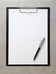 Template of white paper with a ballpoint pen on light grey concrete background in a black tablet with a clip. Concept of new idea, business plan and strategy, with empty space for text