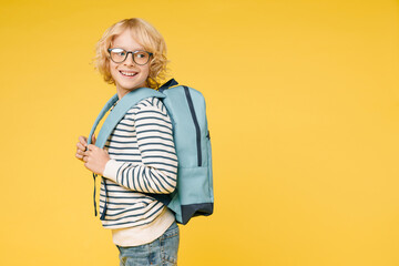 Side view of funny little male kid teen boy 10s years old in casual striped sweatshirt eyeglasses backpack looking aside isolated on yellow color background, child studio portrait. Education concept.
