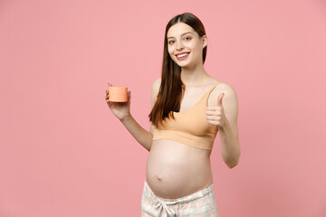 Fototapeta na wymiar Pregnant woman future mom in top with belly stomach tummy with baby hold applying cream for stretch marks striae isolated on pink background studio Maternity family pregnancy expectation concept