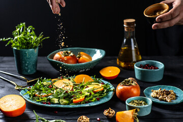 man following recipe on digital tablet and cooking fresh tasty persimmon salad with arugula, avocado, pumpkin seeds, walnuts, pomegranate, Freezer food prepare in process