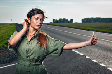 sexy adorable woman in a tight overalls is trying to catch a car on the road, portrait