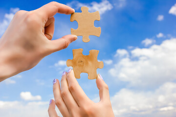 Male and female hand, holding two halves of one puzzle, against a background of blue sky and...