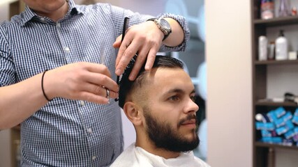 Young man in barber shop sits in an armchair. Barber cuts his hair with a trimer.