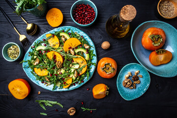 Fresh Tasty Persimmon salad with arugula, avocado, pumpkin seeds, walnuts, pomegranate, Healthy vegan food, top view