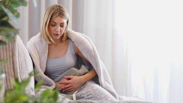 Stomach ache. A young woman warms her aching belly with a hot water bottle. Menstrual pain, colic and stomach discomfort. 