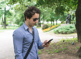 Young man looking on his android phone in city park