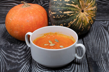 Pumpkin tomato cream soup. With the addition of pumpkin seeds. Several pumpkins are nearby. On pine boards.