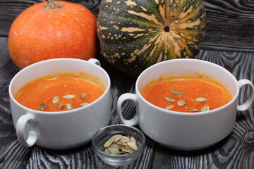 Pumpkin tomato cream soup. With the addition of pumpkin seeds. Several pumpkins are nearby. On pine boards.