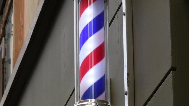 Barber pole rotating on wall outside hairdresser shop. Retro barbershop and hairdresser symbol in shape of spinning spiral inside glass pole. Traditional French style striped barber pole rotation