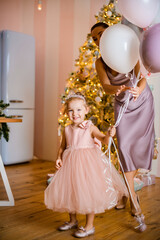little funny girl in pink dress stands with balloons in her hand