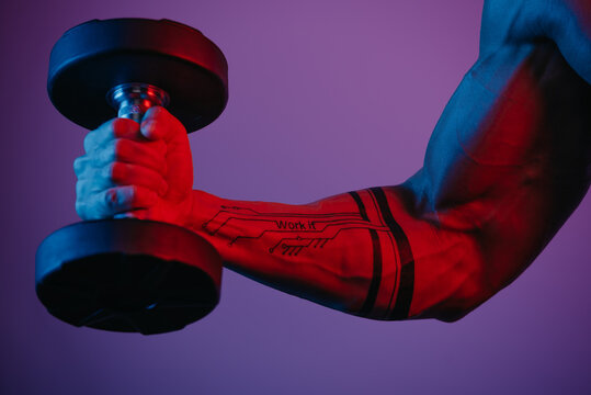 A close photo of a muscular arm which is doing bicep curls with a dumbbell under blue and red lights. A man's forearm with a tattoo: Work it.