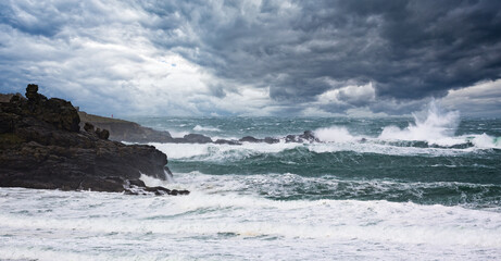 Fototapeta na wymiar Dramatic stormy sea and thunderous sky with large waves crashing onto rocks