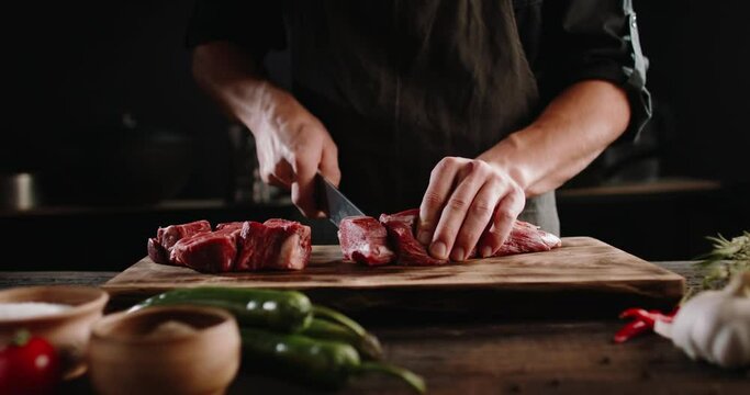 Chef cutting meat with a knife on kitchen table. Cooker is making a meal out of beef and vegetables on professional kitchen 4k footage