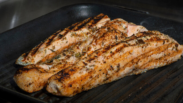 Pescado cocinado dorado en plancha caliente negra hirviendo con condimento de or&eacute;gano verde algunos pedazos de pimienta 