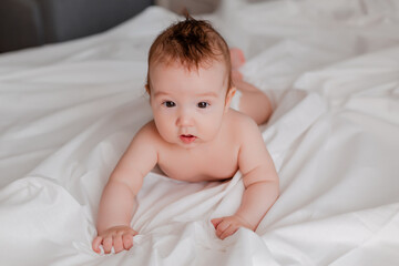 baby boy 4 months lies on the bed with a white sheet, space for text.