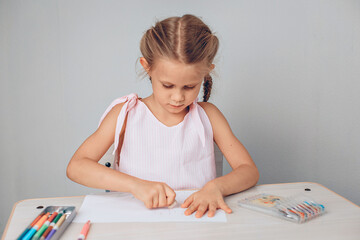 Portrait of an amazing beautiful intelligent girl sitting at a white table and taking pencils in her hands for drawing on paper. Focus concept