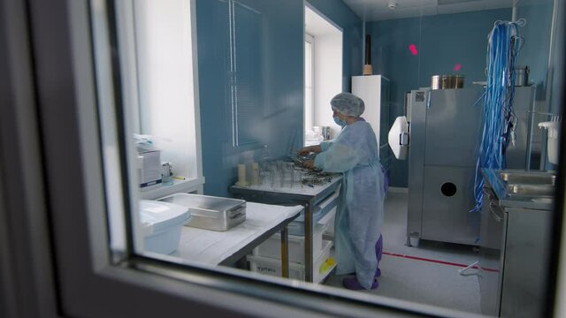 Full through window footage of unrecognizable nurse in sterile clothing sterilizing surgical instruments for operation